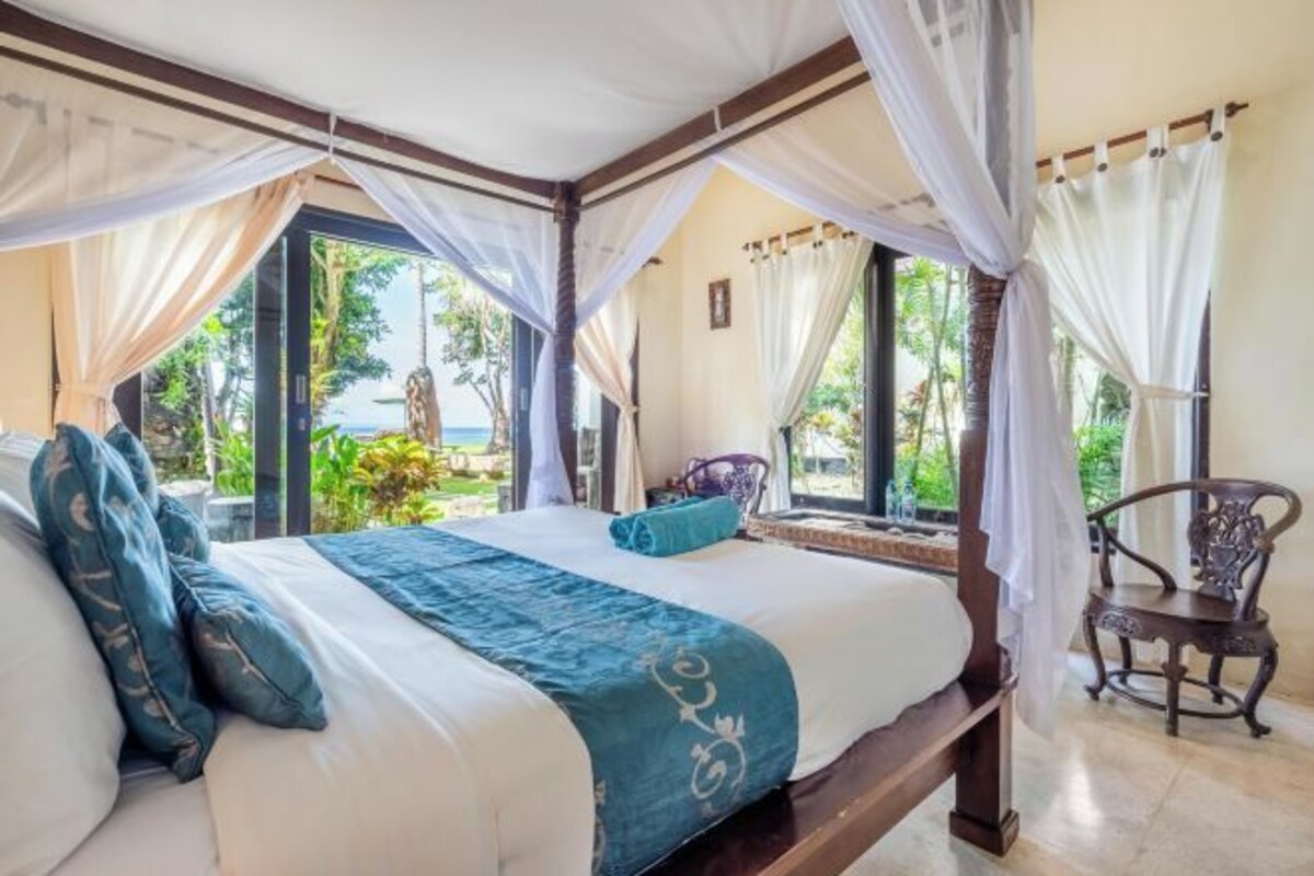 A bedroom with a bed, a chair, and a view of the outdoors.
