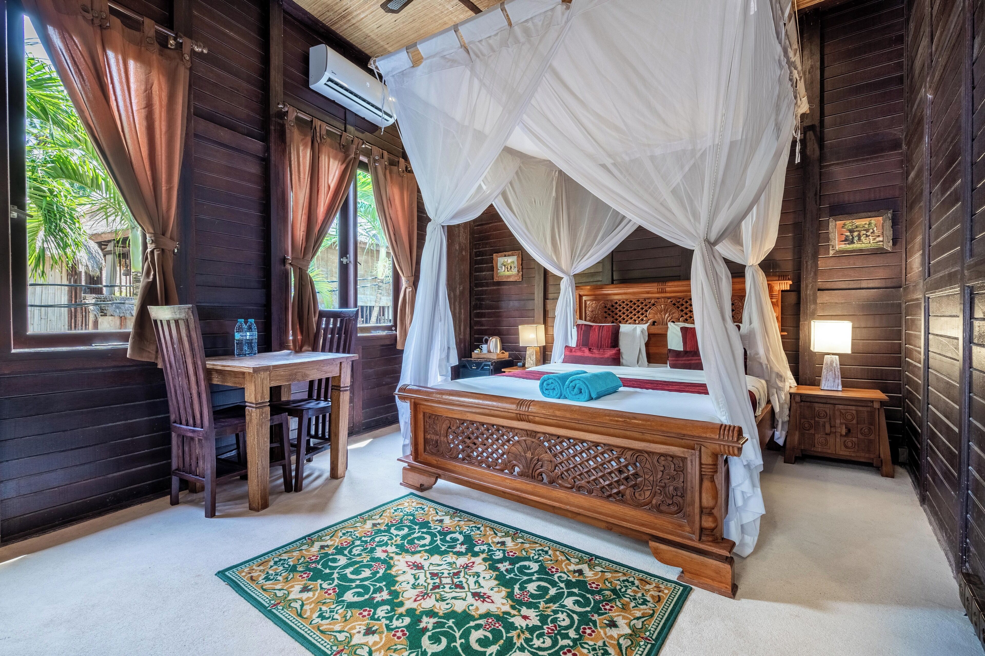 A wooden room with a four-poster bed, a wooden desk, and a chair.
