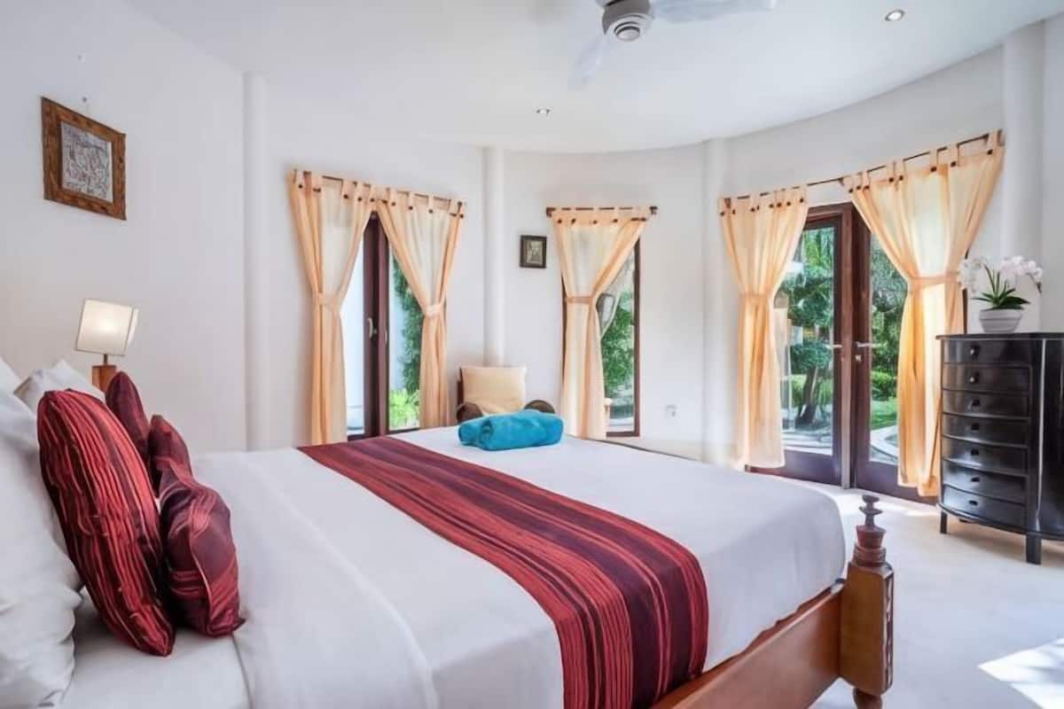 A bedroom with a large bed, a bedside table with a lamp, and a dresser.
