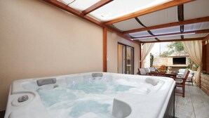Un jacuzzi bajo una pérgola con un muro de piedra y zona de estar al aire libre.