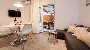 Una sala moderna con un sofá, una mesa de comedor con sillas, un televisor montado en la pared y un ventanal corredizo que da a una zona de comedor.