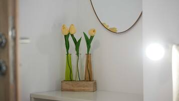 En hvid hylde med tre vaser med gule blomster, en træklods og et spejl monteret på væggen.