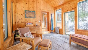 L’intérieur d’un chalet en bois, avec un sol en pierre, des meubles en bois et de grandes fenêtres donnant sur le paysage extérieur.