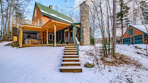 Une cabane en rondins avec une cheminée en pierre, une terrasse en bois et un escalier menant à l’entrée.