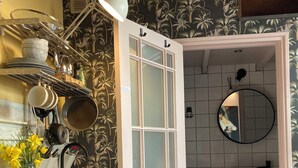 Una cocina con una puerta blanca, una estantería con vajilla, un hervidor y un florero con flores.