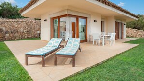 Een huis met een terras, twee lounge stoelen, een tafel met stoelen en een stenen muur.