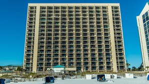 A high-rise hotel with multiple balconies, a beachside location, and a clear blue sky.