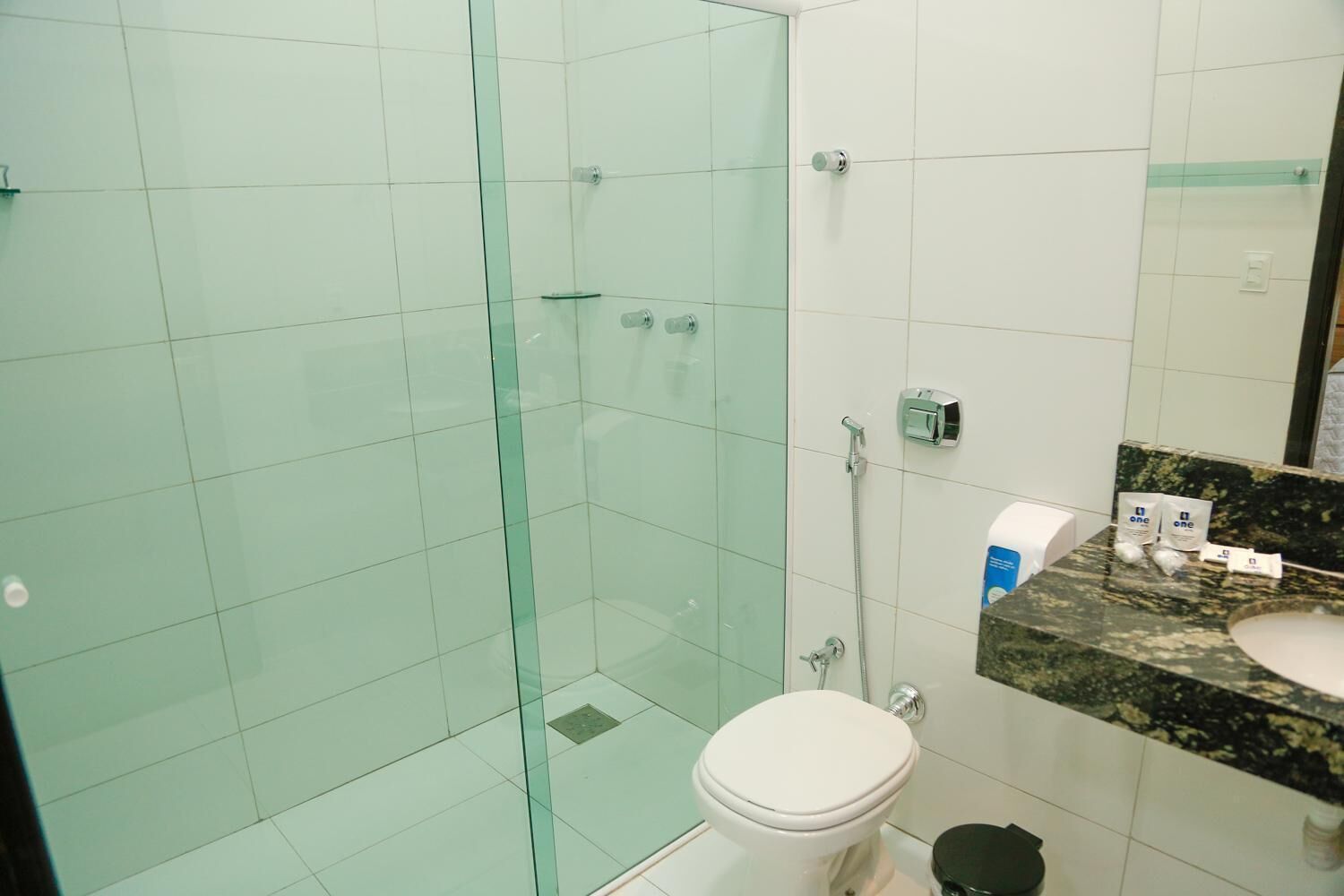 Et badeværelse med et glasbadeafskærmning, et hvidt toilet og en vask med bordplade i granit.