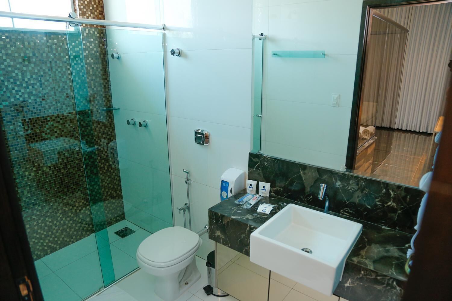 A bathroom with a glass shower enclosure, a toilet, a sink with a marble countertop, and a mirror.