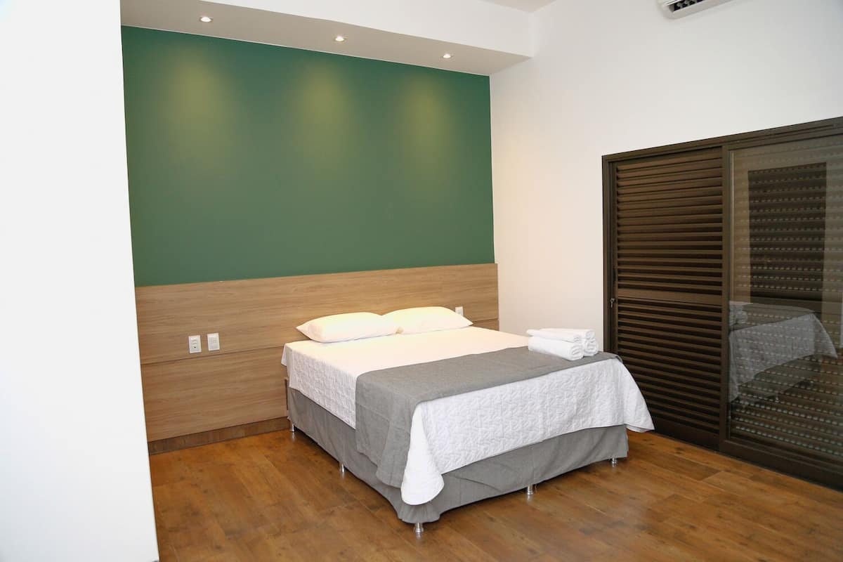 Un lit bien fait, avec une couverture grise et des oreillers, une tête de lit en bois et un mur d’accent vert.