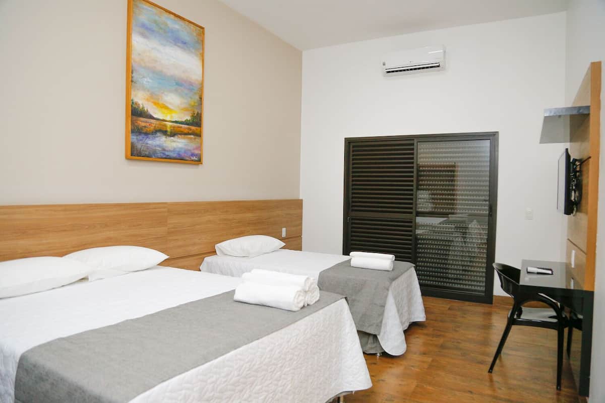 Une chambre d’hôtel avec deux lits, un bureau et une grande fenêtre avec des stores.