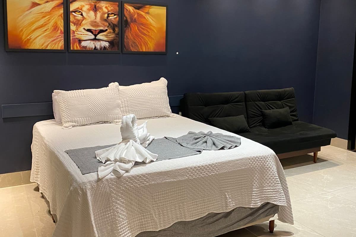 Une chambre moderne avec un grand lit, un mur bleu foncé et trois tableaux encadrés représentant des lions.