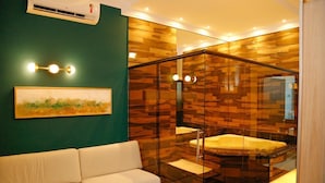 Un baño moderno con un jacuzzi con mampara de vidrio, un sofá blanco y un cuadro enmarcado en la pared.
