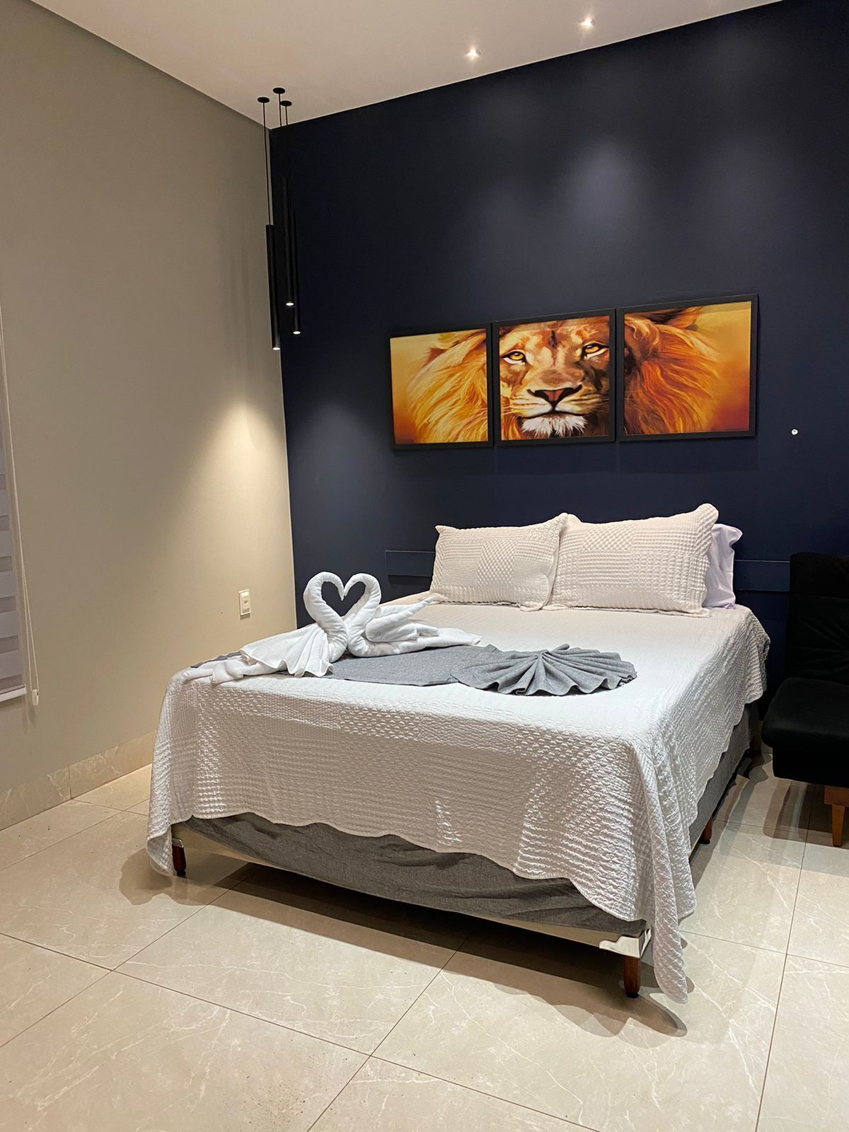 A modern bedroom with a bed, a dark wall, and three framed lion paintings.