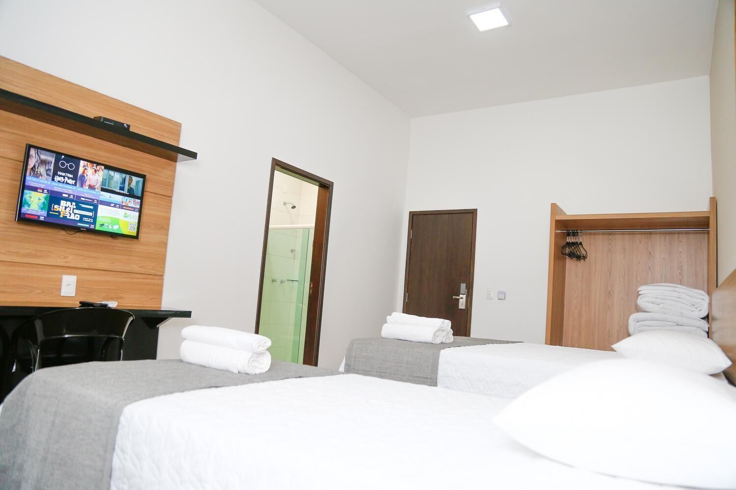 Une chambre d’hôtel avec deux lits, un téléviseur fixé au mur, une armoire en bois et un espace douche.