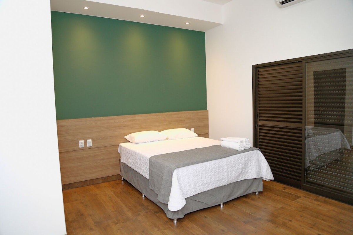 Un lit bien fait, avec une couverture grise et des oreillers, une tête de lit en bois et un mur vert.