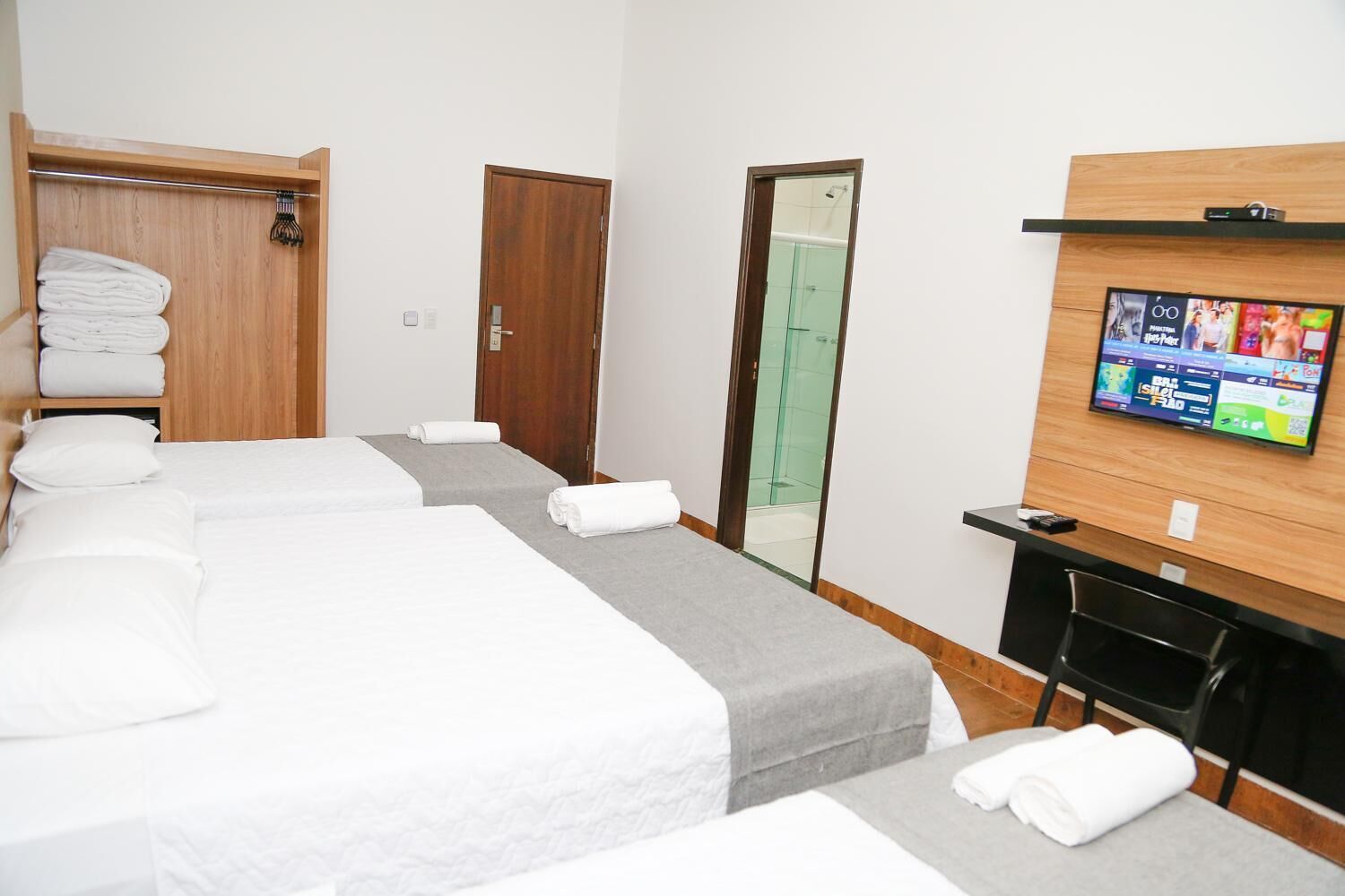 Habitación de hotel con dos camas, un armario de madera, zona de ducha y televisor en la pared.