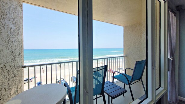 Un balcon avec vue sur la plage, deux chaises et une table.