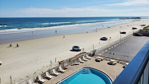Une vue sur la plage avec une piscine, des chaises longues et une jetée en arrière-plan.