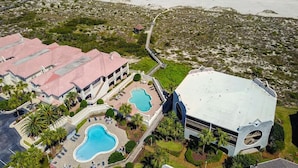 Ett flygbildsbild av ett semesterområde med flera byggnader, en swimmingpool och en strand.