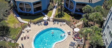 A pool area with lounge chairs and umbrellas, surrounded by buildings with a unique octagonal shape and a swimming pool.