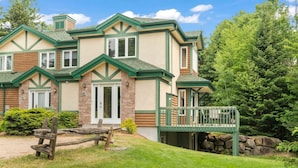 A two-story house with a green and beige exterior, a stone foundation, and a covered porch.