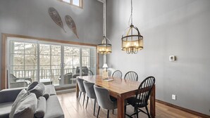 Un espace repas avec une table et des chaises en bois, un luminaire suspendu et une vue dégagée grâce à de grandes fenêtres.