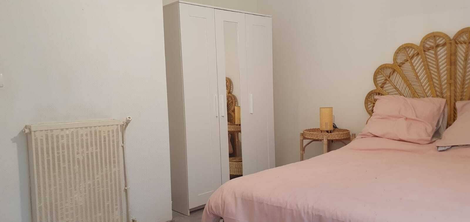Une chambre à coucher avec un lit, une armoire, un radiateur et une chaise en osier.