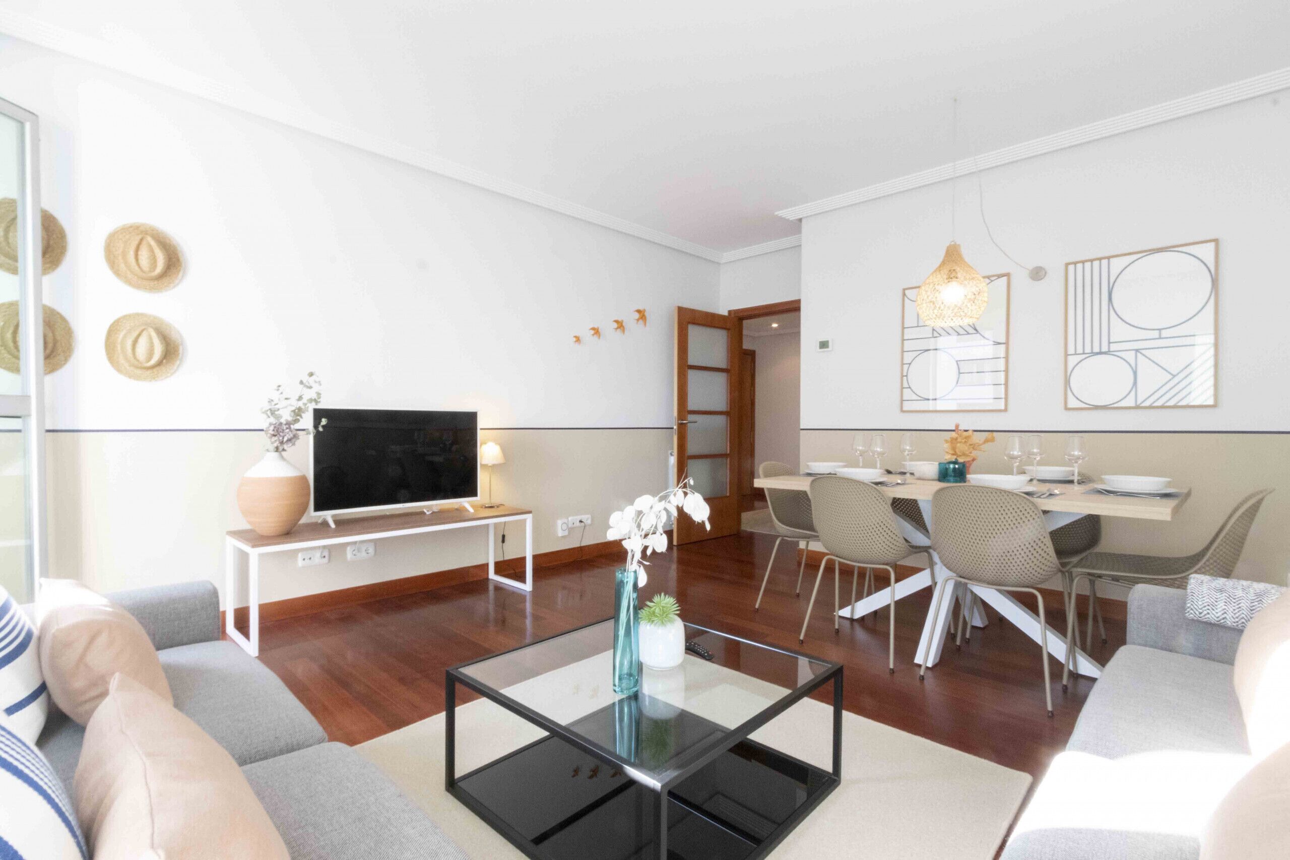Un salon moderne doté d’un téléviseur à écran plat, d’une table basse en verre et d’un coin repas avec une table et des chaises.