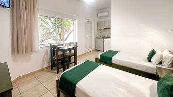 Habitación de hotel con dos camas, una mesita, una silla, ventana con vistas a árboles y una kitchenette.
