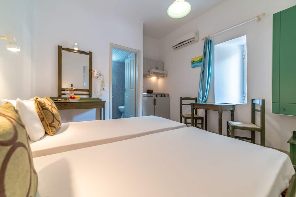 Habitación de hotel con una cama grande, un escritorio con una silla, una kitchenette pequeña y un baño visible a través de una puerta abierta.