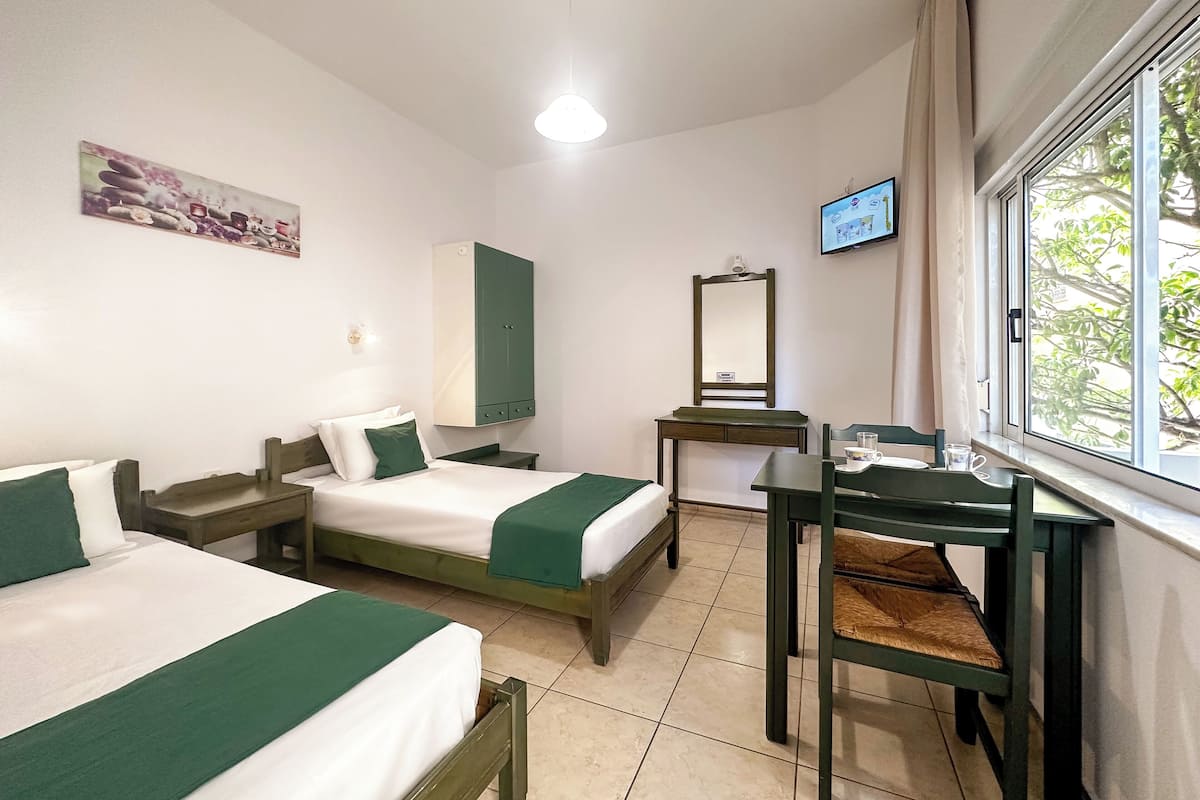 Habitación de hotel con dos camas, un escritorio, una silla, un televisor, una ventana y un cuadro en la pared.