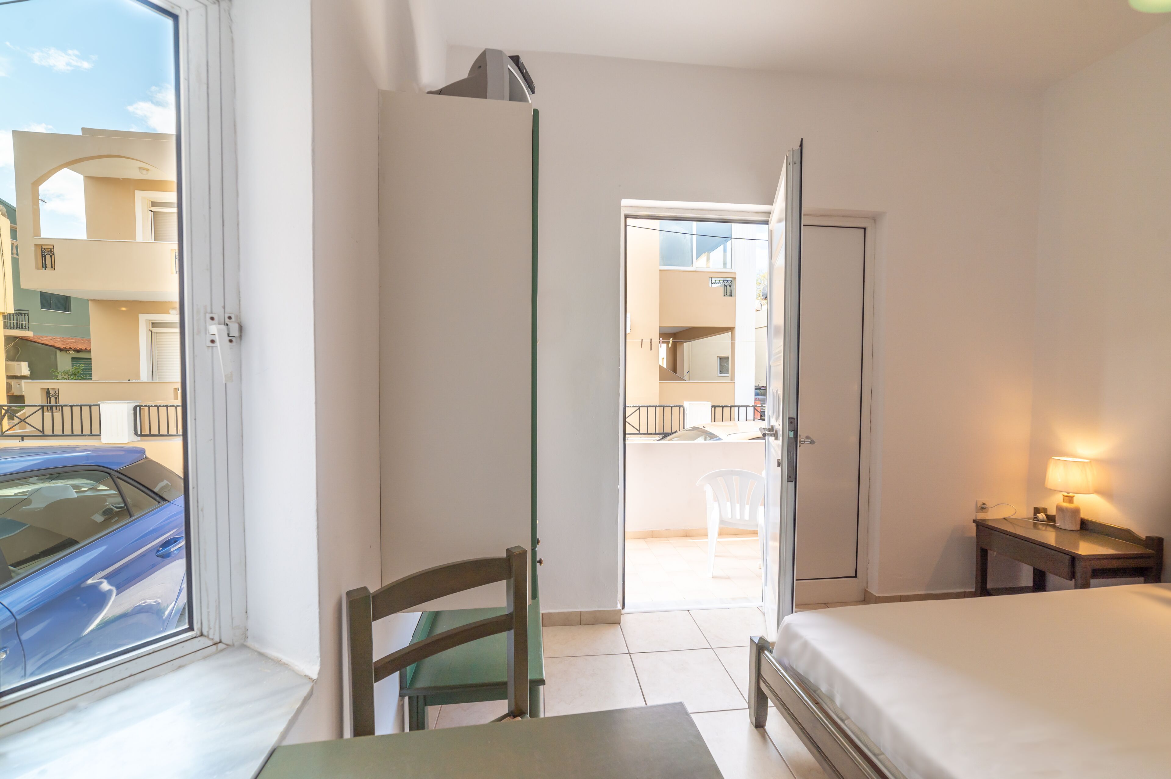 Een hotelkamer met een bed, een tafel, een stoel, een lamp en uitzicht op het balkon.