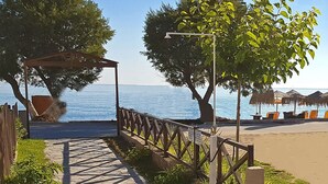 Un chemin de pierres menant à une zone de plage, agrémentée d’une clôture en bois, d’une pergola et de chaises de plage.