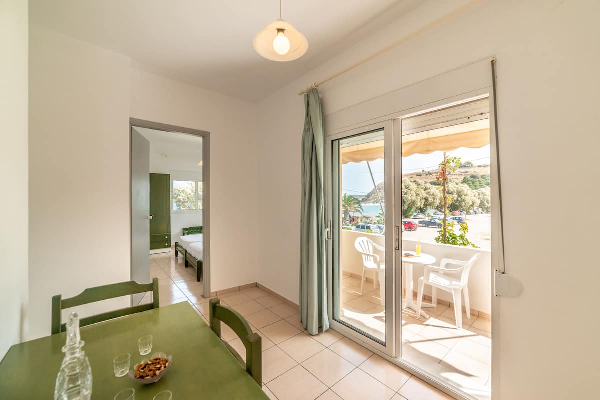 Una habitación con una mesa de comedor, sillas, una cama y una puerta corrediza de vidrio que da a un área exterior con vistas a un estacionamiento y árboles.