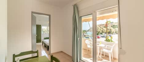 Una habitación con una mesa de comedor, sillas, una cama y una puerta corrediza de vidrio que da a un área exterior con vistas a un estacionamiento y árboles.