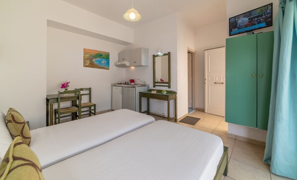A hotel room with a bed, a desk, a chair, a small kitchenette, a mirror, and a TV. - Akti Galinis (Apokoronas)