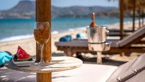 Une table installée sur la plage, avec un verre de vin, une tranche de pastèque et une bouteille de champagne.