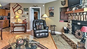 A living room with a fireplace, a leather armchair, a glass coffee table, and a television mounted above the fireplace. - Sunrise Above Ober, Hot Tub and Two Decks (Gatlinburg)