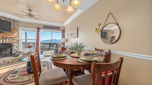 A dining area with a round table set for six, surrounded by wooden chairs. A stone fireplace is visible in the background, and a television is mounted on the wall. - Sunrise Above Ober, Hot Tub and Two Decks (Gatlinburg)