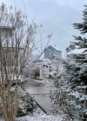 Winter wonderland scene with houses, a driveway, and a serene body of water surrounded by trees.