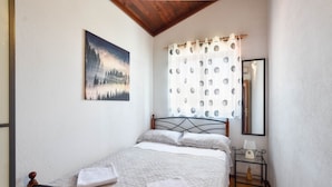 Une chambre à coucher avec un lit, un tableau, un rideau, une table de chevet avec une lampe et un miroir.