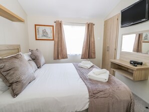 A hotel room with a bed, a television, a wardrobe, and a window with curtains. - Superb Detached Lodge Located on Skipsea Sands (Driffield)