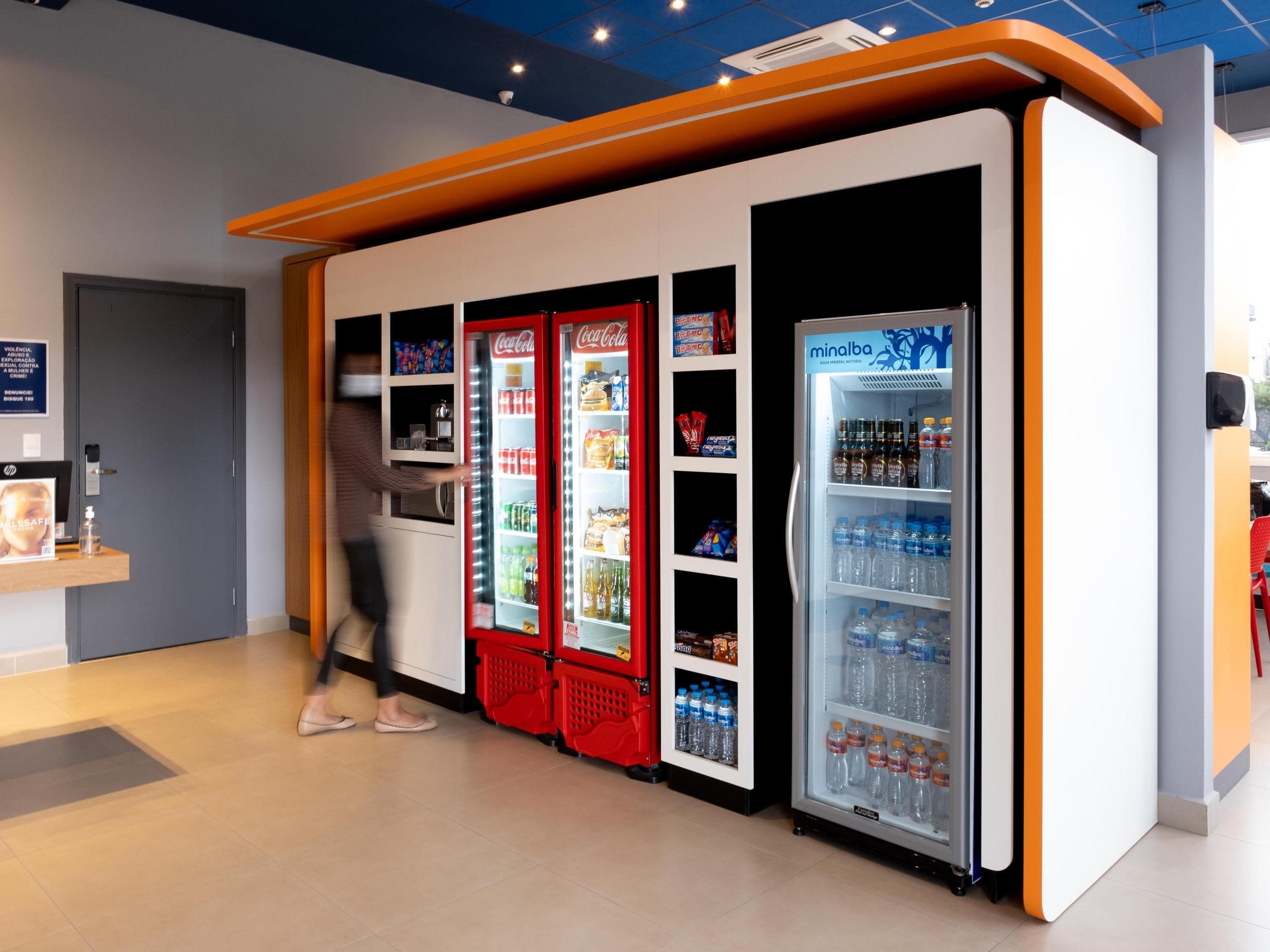 Un vestíbulo de hotel moderno con máquinas expendedoras, un refrigerador de Coca-Cola y un dispensador de agua Minalba.