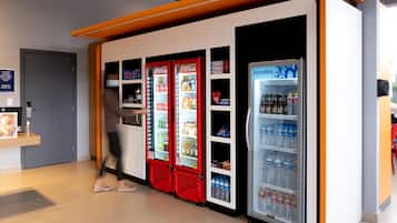 Un vestíbulo de hotel moderno con máquinas expendedoras, un refrigerador de Coca-Cola y un dispensador de agua Minalba.