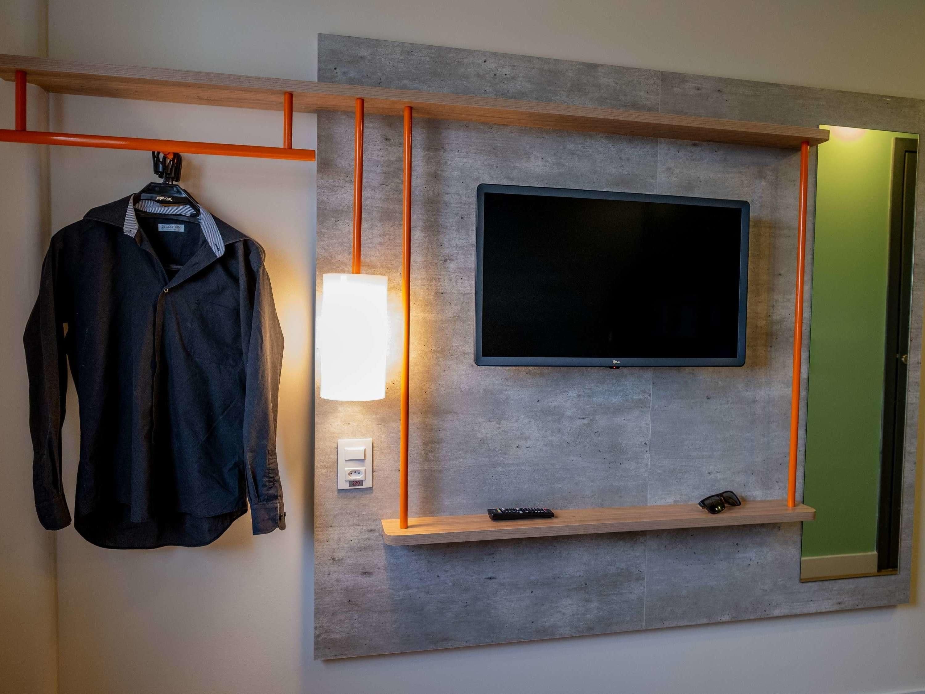 Una habitación moderna con un televisor montado, un perchero y una estantería con un control remoto.