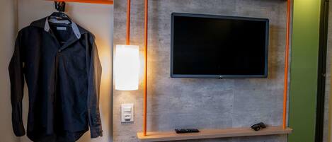 Una habitación moderna con un televisor montado, un perchero y una estantería con un control remoto.