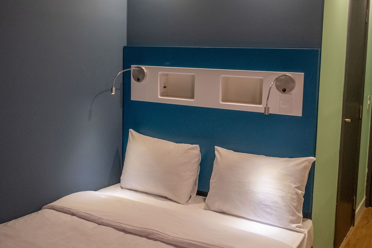 A neatly made bed with white linens in a room with blue walls and a blue headboard.