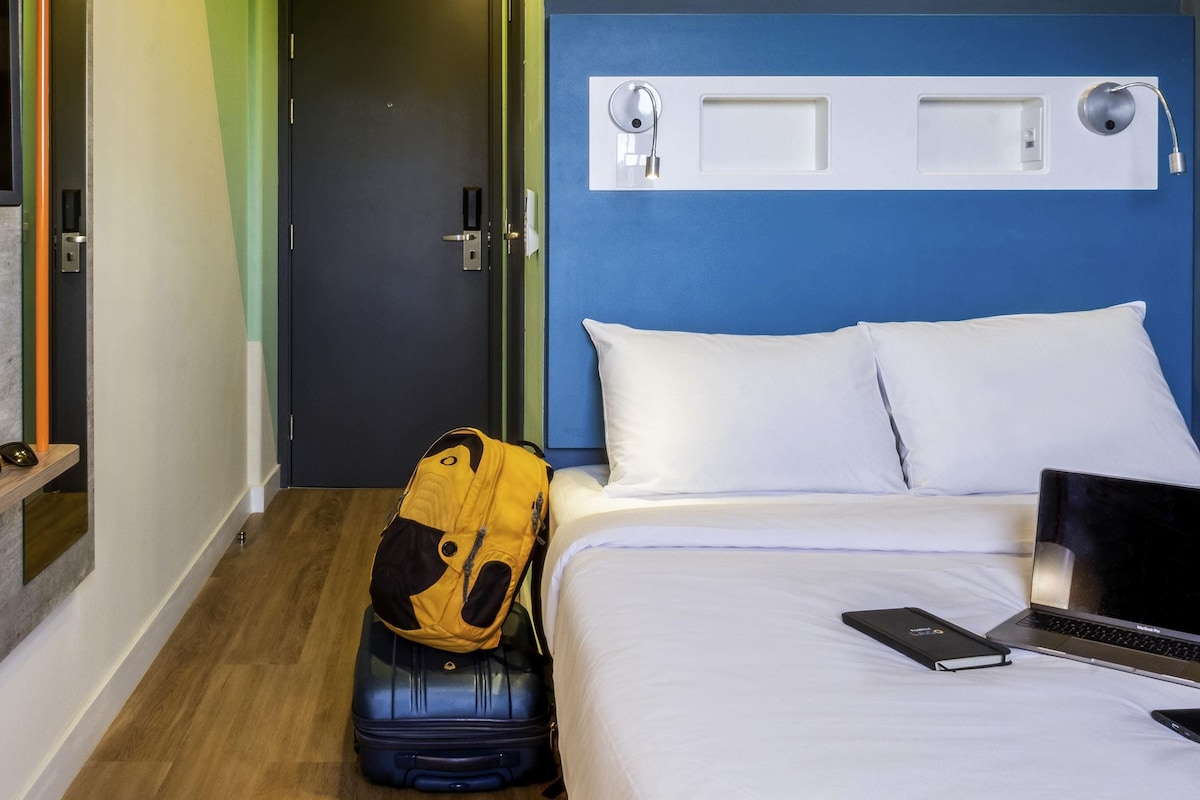A hotel room with a bed, a suitcase, a laptop, and a backpack.
