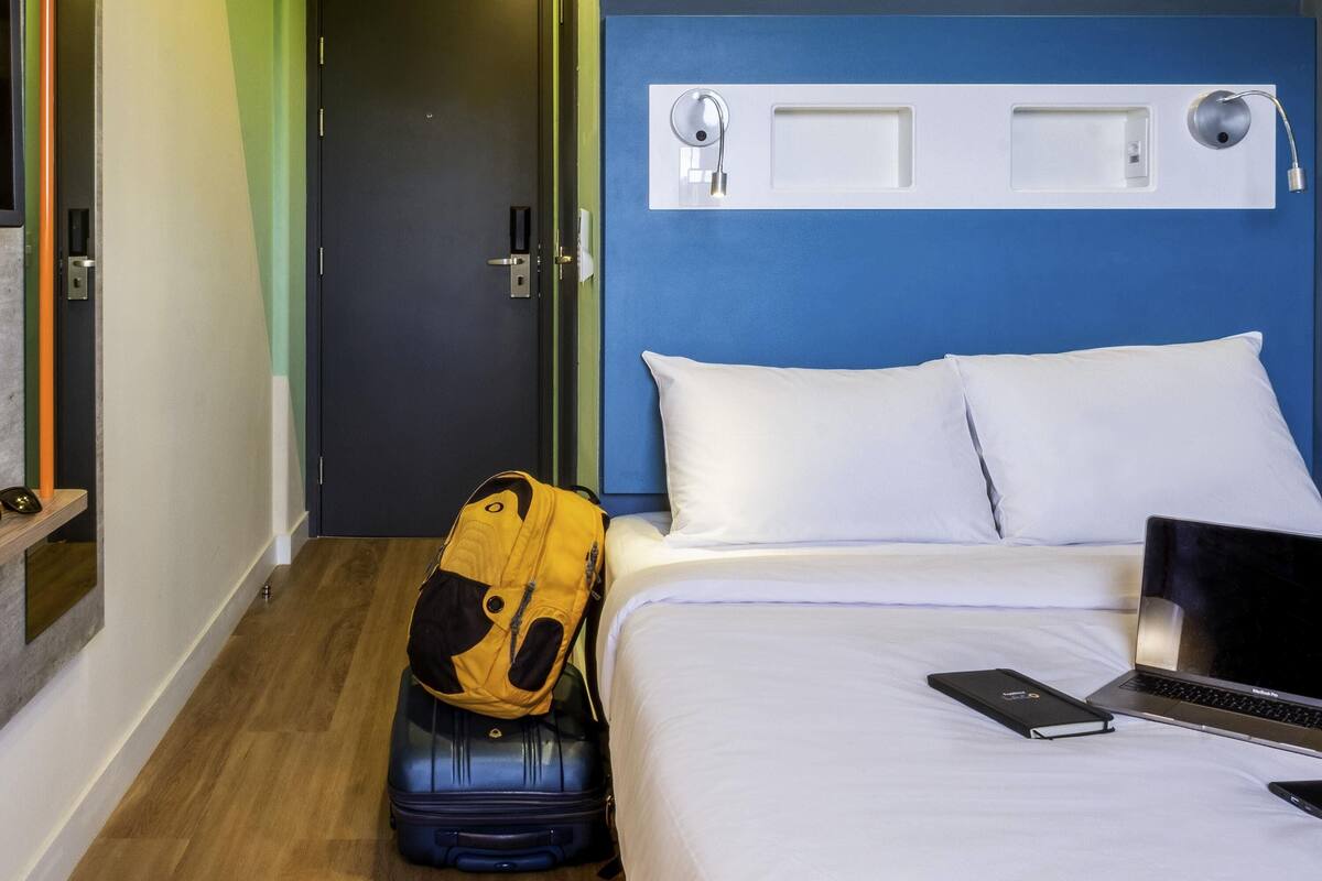 A hotel room with a bed, a suitcase, a laptop, and a backpack.